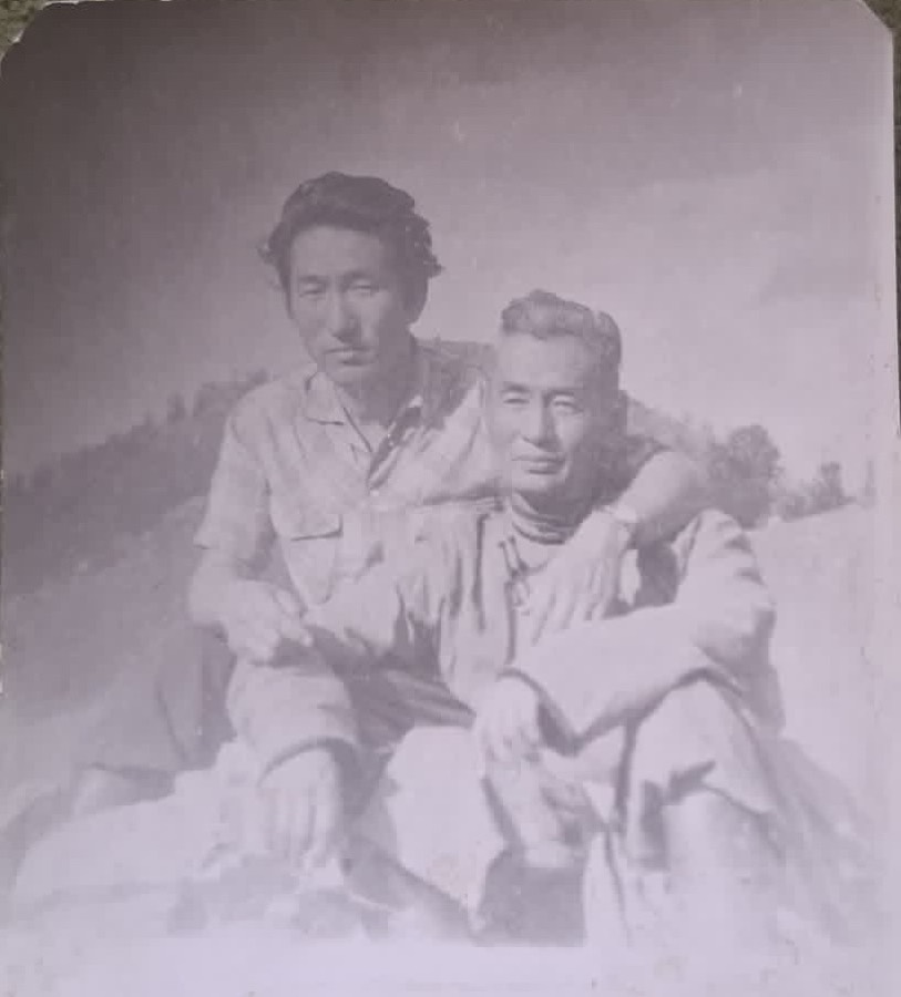 Original badly faded photo of two men sitting on a rock, barely visible